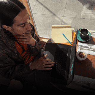 บุคคลหนึ่งขณะทำงานบน MacBook Pro ที่ไม่ได้เสียบปลั๊กในบรรยากาศของร้านกาแฟ